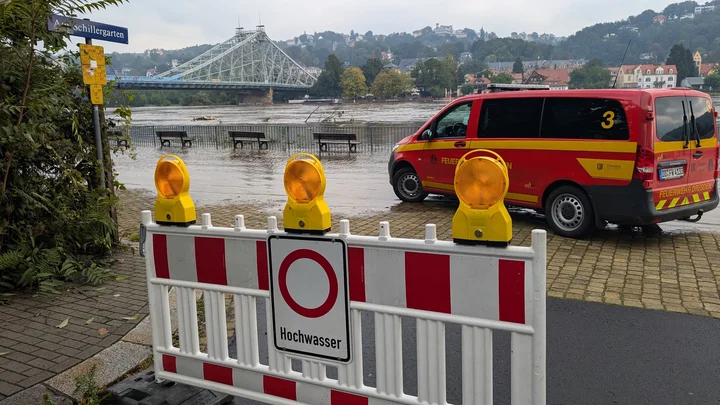 Fahrzeug der Feuerwehr Dresden hinter einer Absperrung "Hochwasser" vor überflutetem Uferbereich